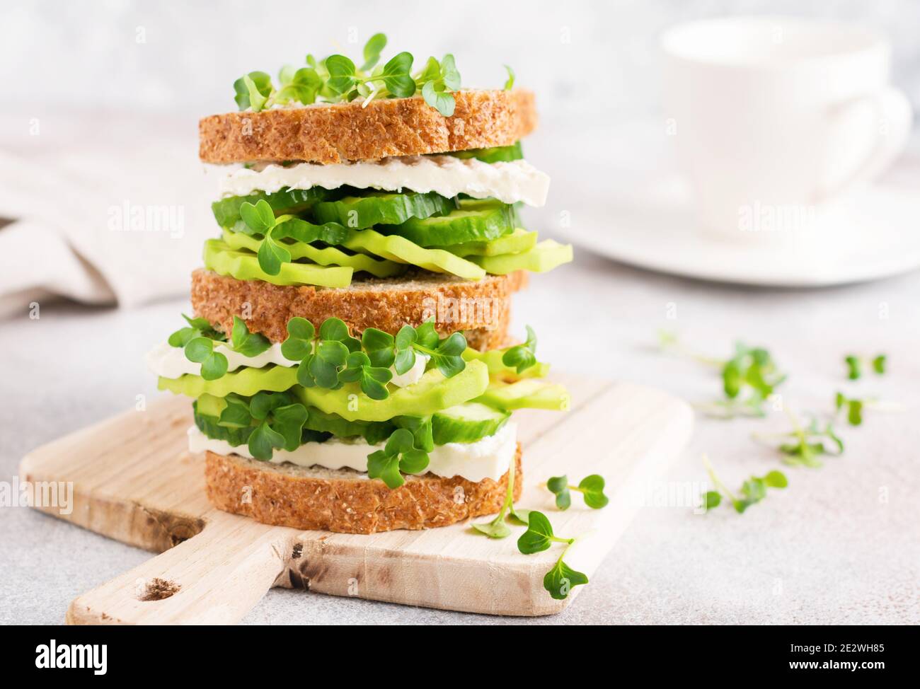 Avocado, cucumber and feta cheese sandwich decorated with micro-greens and multi-grain bread on a simple wooden stand for a healthy breakfast. Selecti Stock Photo
