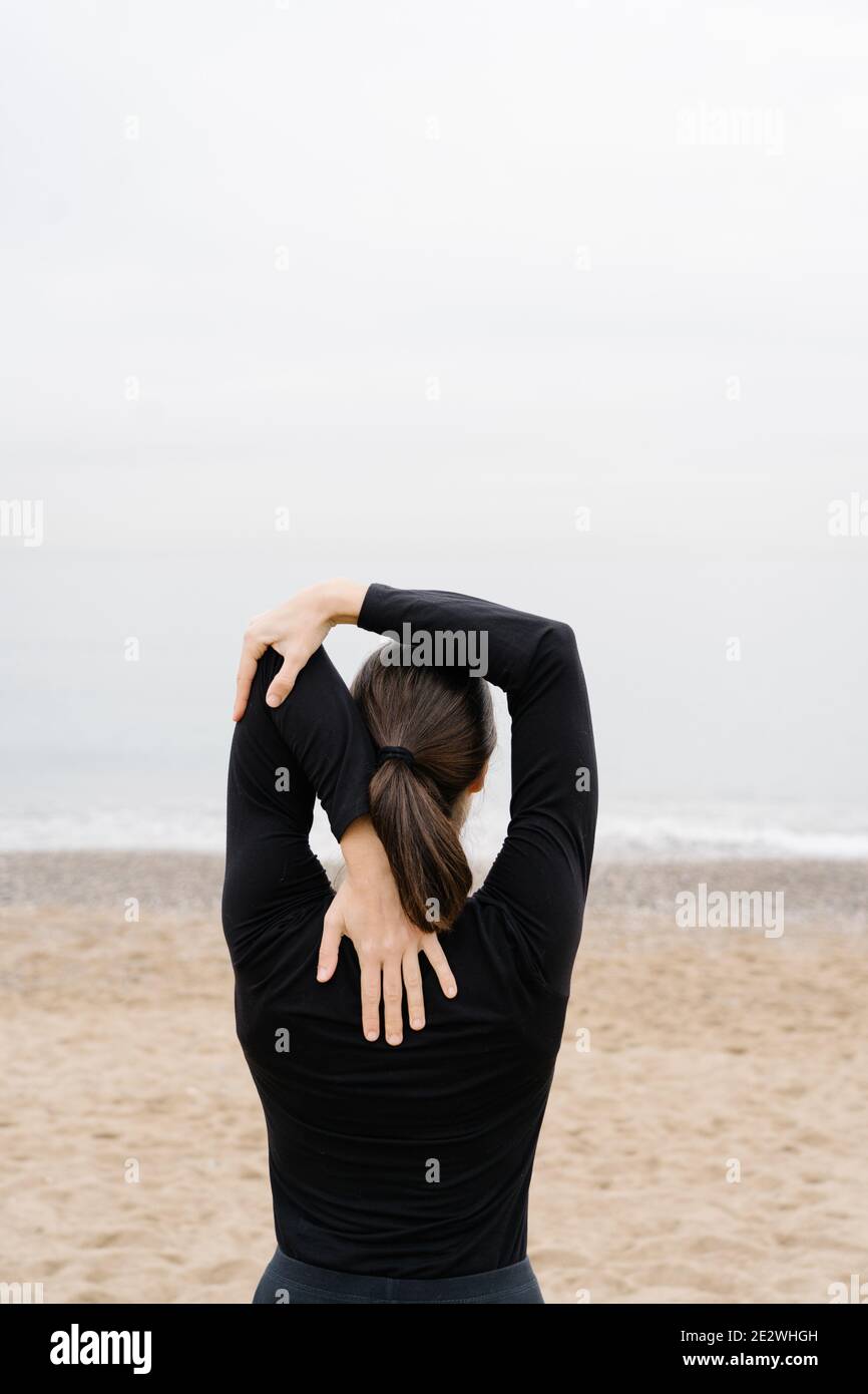 Young woman doing arm stretches as preexercise wain front of the sea