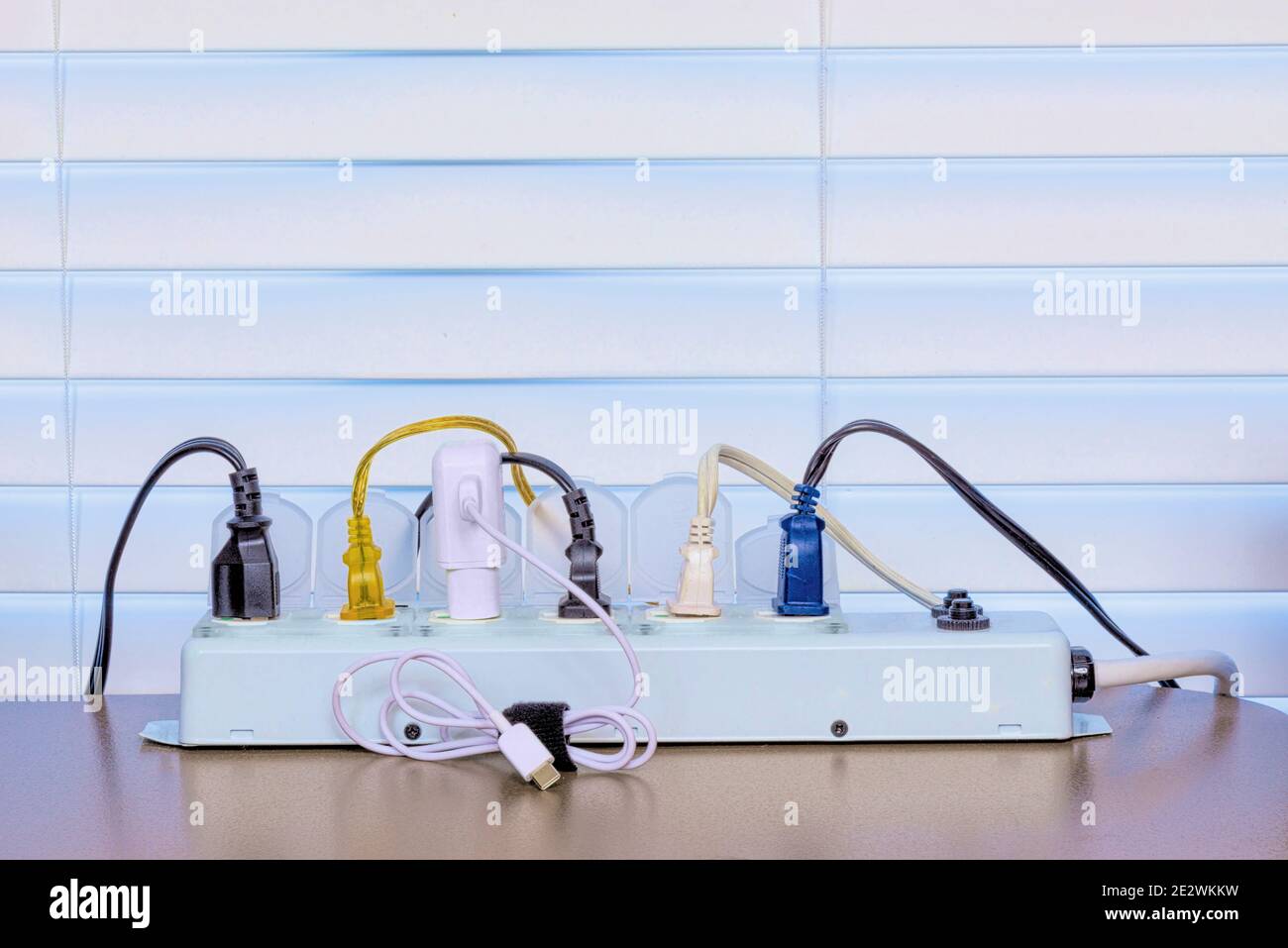 Horizontal shot of a full power strip on a desk in front of a Venetian blind background. Stock Photo