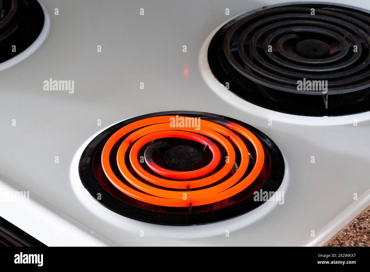 Horizontal shot of a white stove top with one hot burner and two off.  Shot at an angle. Stock Photo