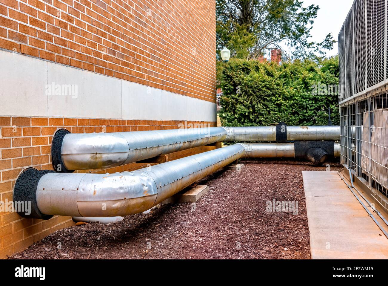 Horizontal shot of HVAC pipes going between outdoor AC units and a residential complex. Stock Photo