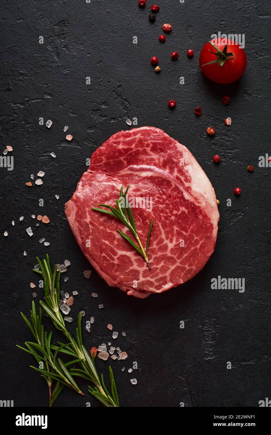 One fresh Parisienne raw steak on white parchment paper with salt, pepper and rosmary in a rustic style on old stone background. Black angus. Stock Photo
