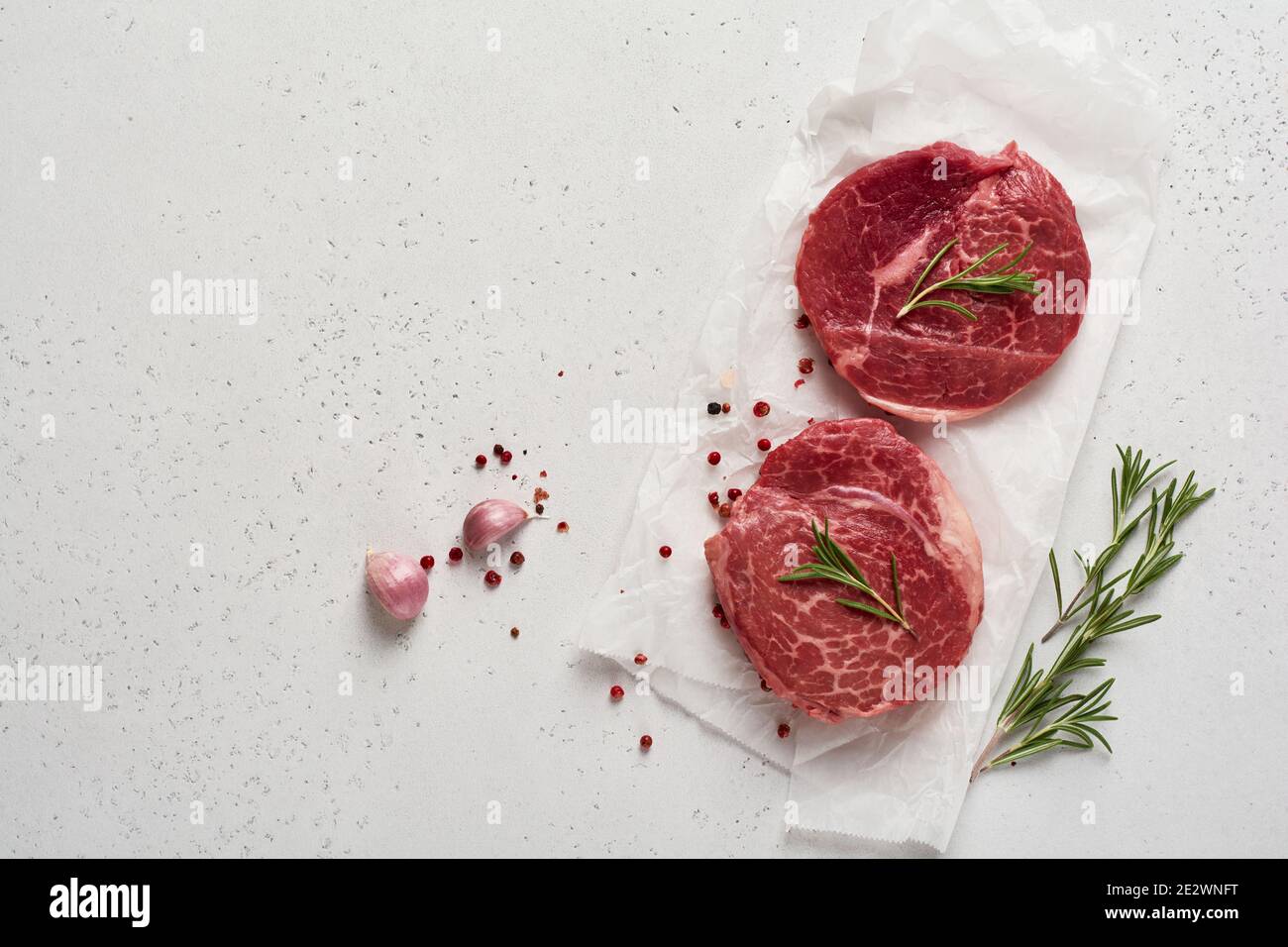 Two fresh Parisienne raw steak on white parchment paper with salt, pepper and rosmary in a rustic style on old wooden background. Black angus. Stock Photo