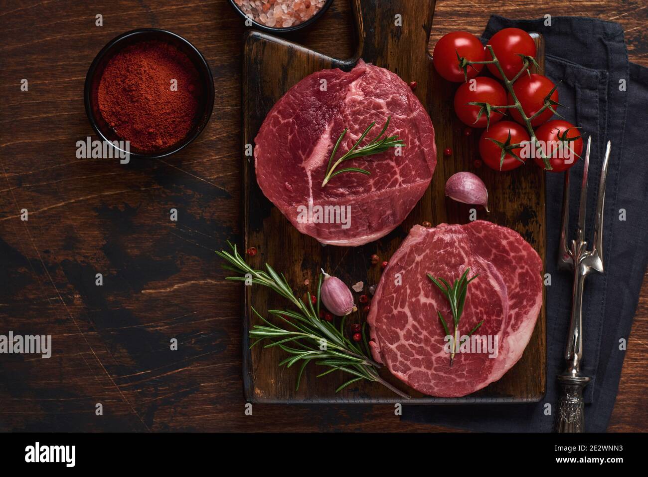 Two fresh Parisienne raw steak on wooden Board with salt, pepper and rosmary in a rustic style on old wooden background. Black angus. Stock Photo