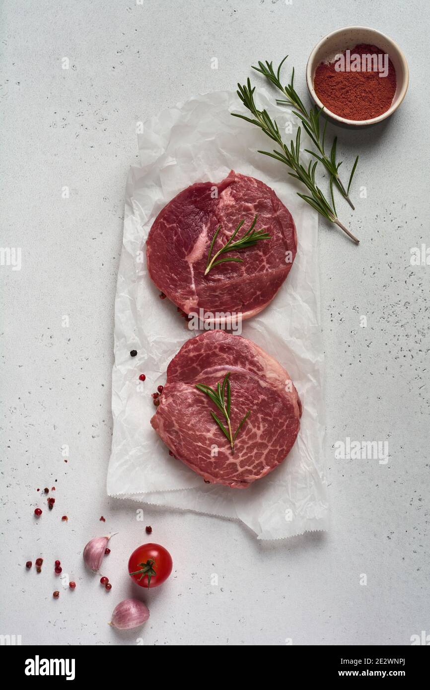 Two fresh Parisienne raw steak on white parchment paper with salt, pepper and rosmary in a rustic style on old wooden background. Black angus. Stock Photo