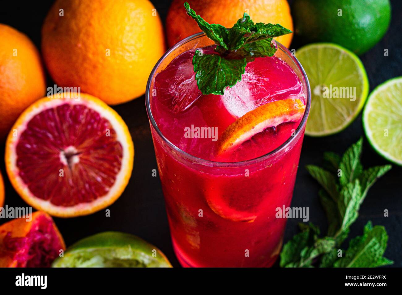 Blood Orange and Raspberry Mojito: A rum cocktail with blood oranges, raspberries, lime, and mint leaves served in a tall glass over ice Stock Photo