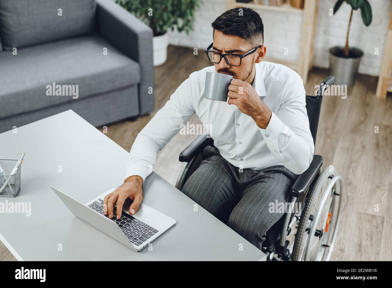 Disabled young businessman drinking coffee at his working table Stock Photo