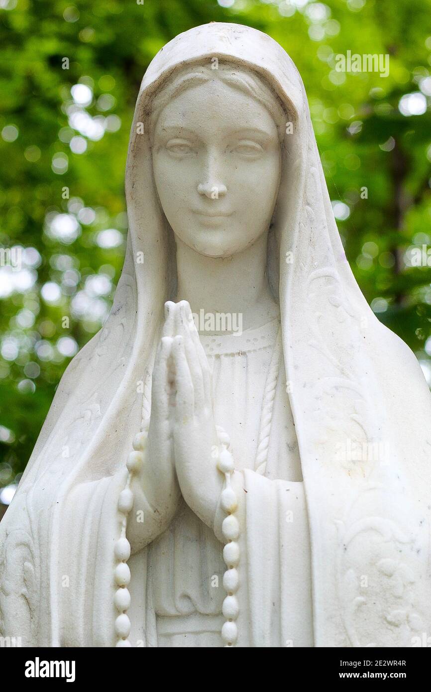 Vertical shot of a Virgin Mary Statue in a garden with a blurry