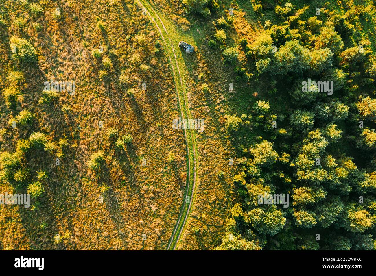 Aerial View Of Car Near Country Road Thgrough Forest And Green Meadow Landscape In Sunny Summer Morning. Top View Of Beautiful European Nature From Stock Photo