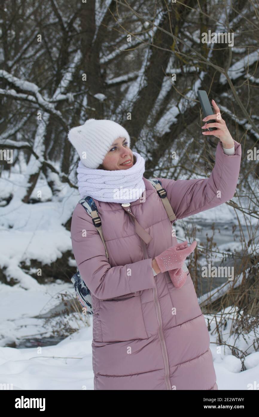A woman in winter clothes walks in the park. Takes a selfie. There