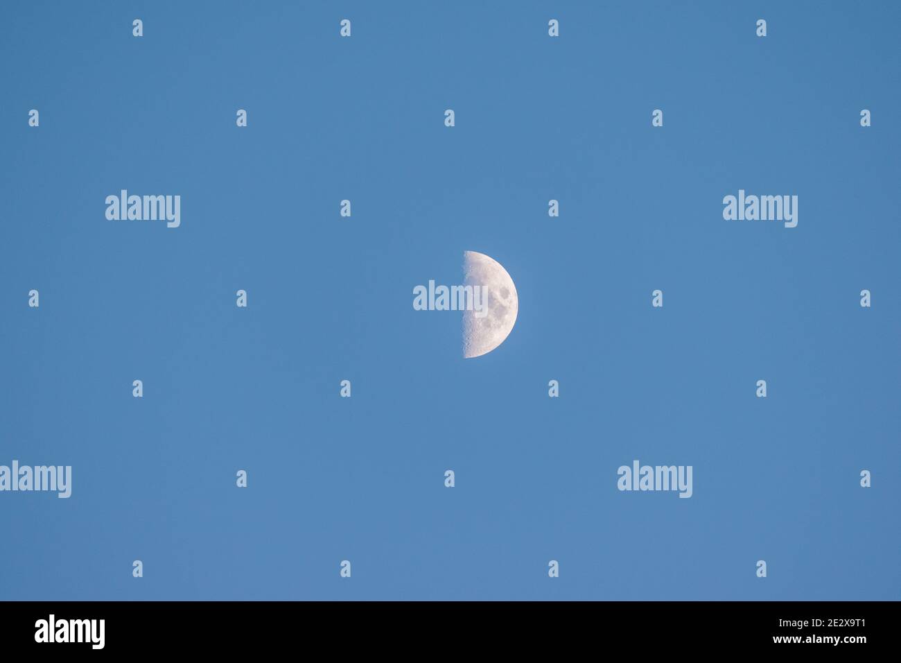Close-up of a quarter moon in a clear, cloudless blue sky at sunset, Ericeira, Portugal. Stock Photo