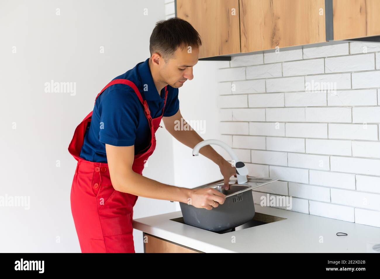 Plumber putting a silicone sealant to installing a kitchen sink Stock