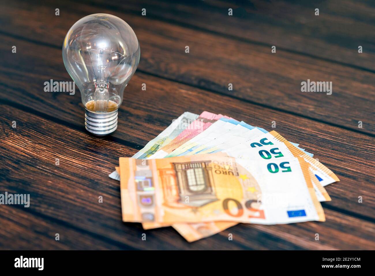 On a wooden background there is a light bulb and money in the form of several bills. Stock Photo