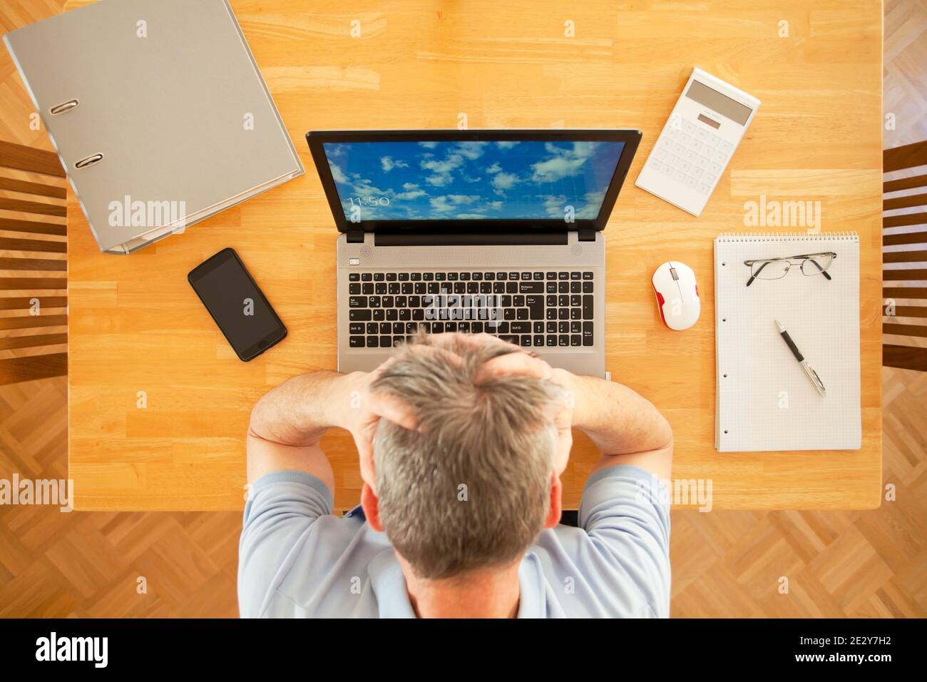 Stressed man sitting at a table with laptop while working from home - overhead view - the photo an the sreen was taken by me Stock Photo