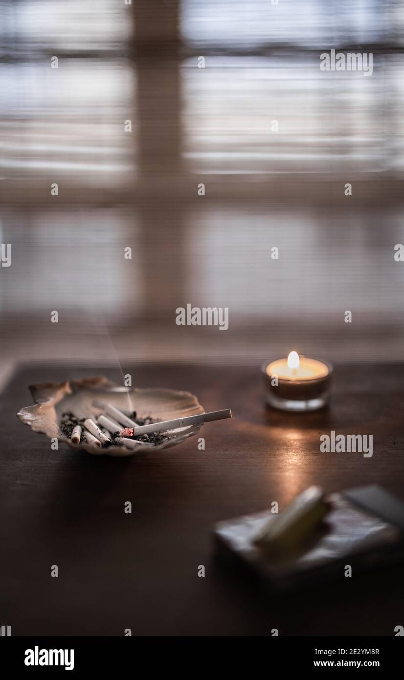 Vertical shot of an ashtray full of burnt cigarettes and a burning
