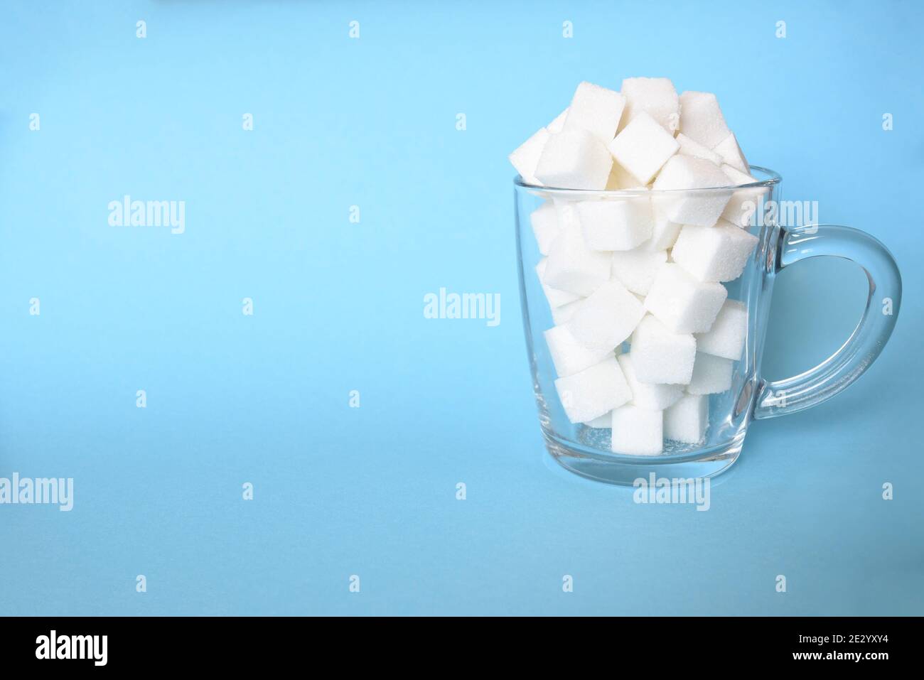 Transparent mug full of refined white sugar cubes on blue background. Copy space Stock Photo