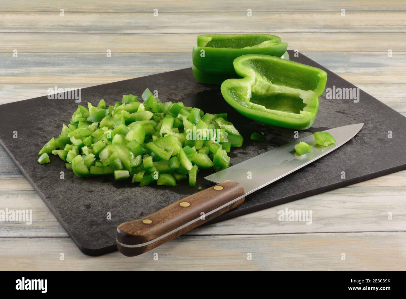 Chopping green bell peppers on black cutting board with kitchen knife ...