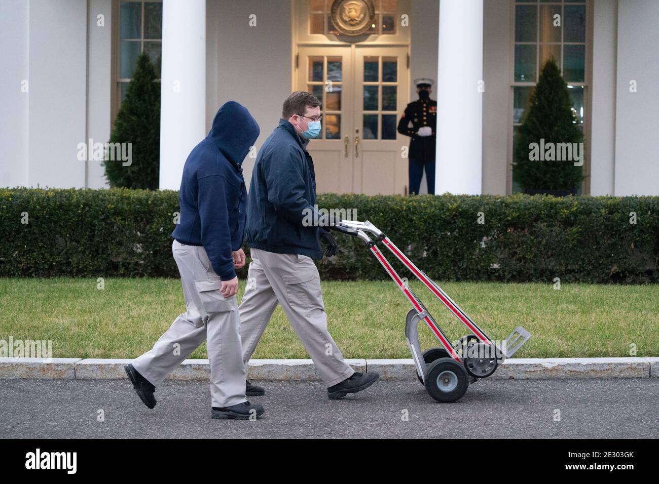 Workers with empty hand trucks pass the West Wing of the White House in Washington, DC on Friday, January 15, 2021. The guard outside the door in the background indicates United States President Donald J. Trump is in the Oval Office.Credit: Chris Kleponis/Pool via CNP | usage worldwide Stock Photo