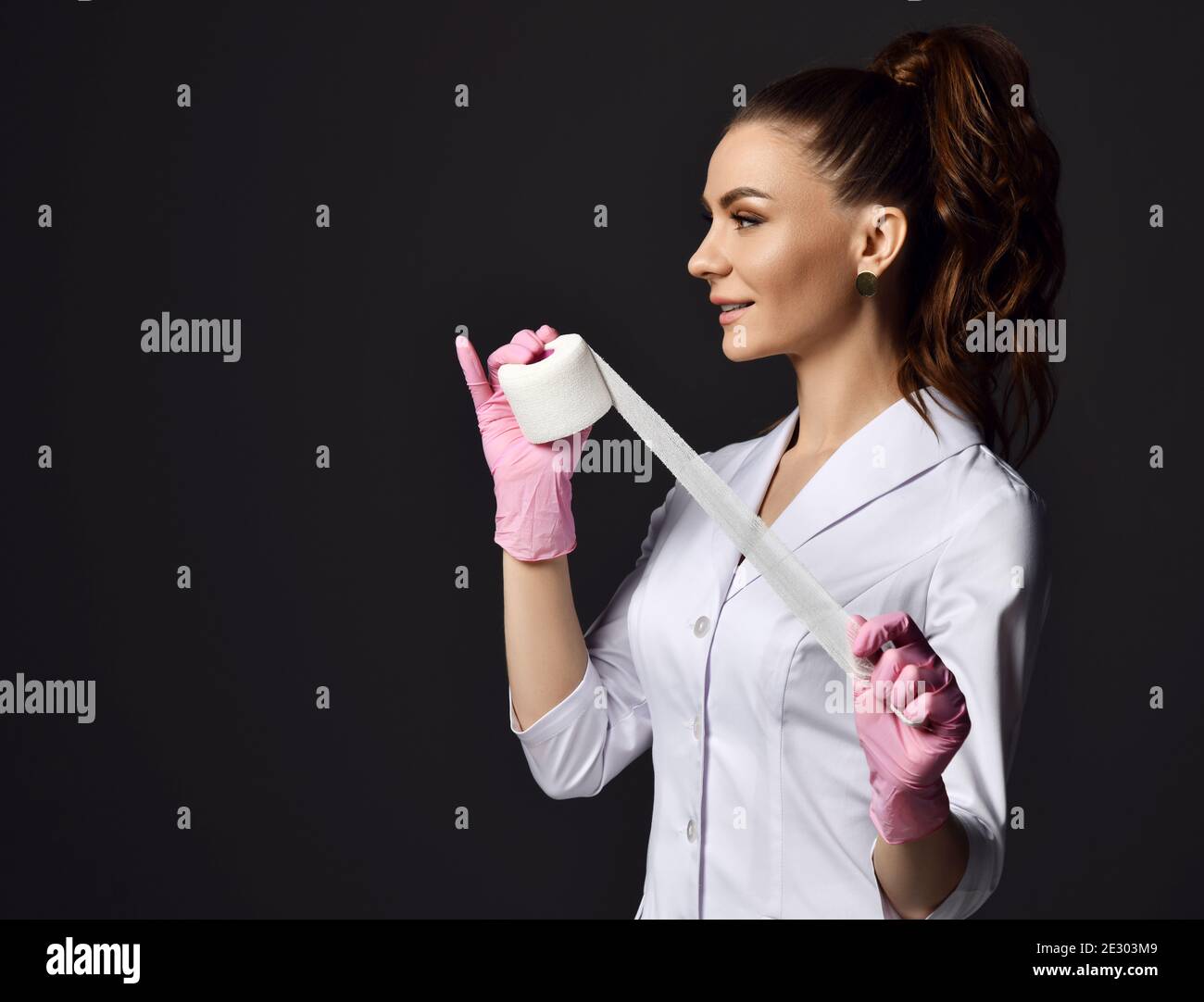 Profile of pretty woman doctor gynecologist or nurse in pink latex gloves and uniform stands holding medical bandage Stock Photo