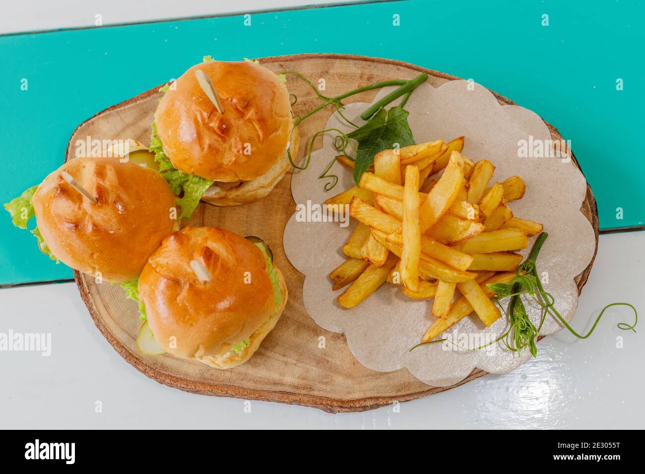 Three fish sliders (mini burgers) with lettuce, tomato and pickles, served with french fries on a wooden tray. Top view. Stock Photo