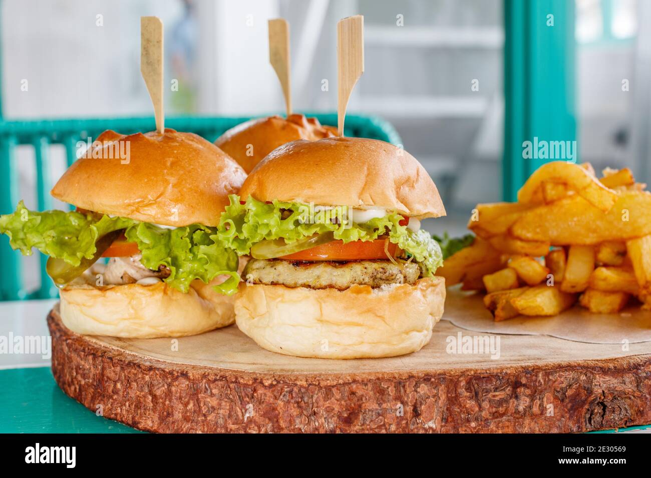 Three fish sliders (mini burgers) with lettuce, tomato and pickles, served with french fries on a wooden tray. Stock Photo