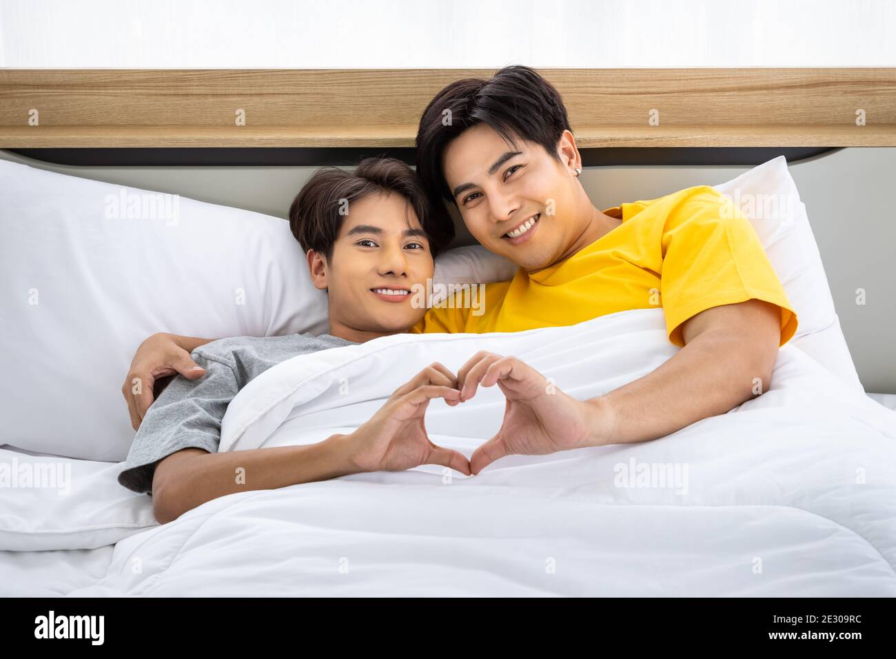Happy Asian homosexual gay men male couple lying and embracing on bed. LGBT and sexual diversity concept. Looking at camera. Stock Photo
