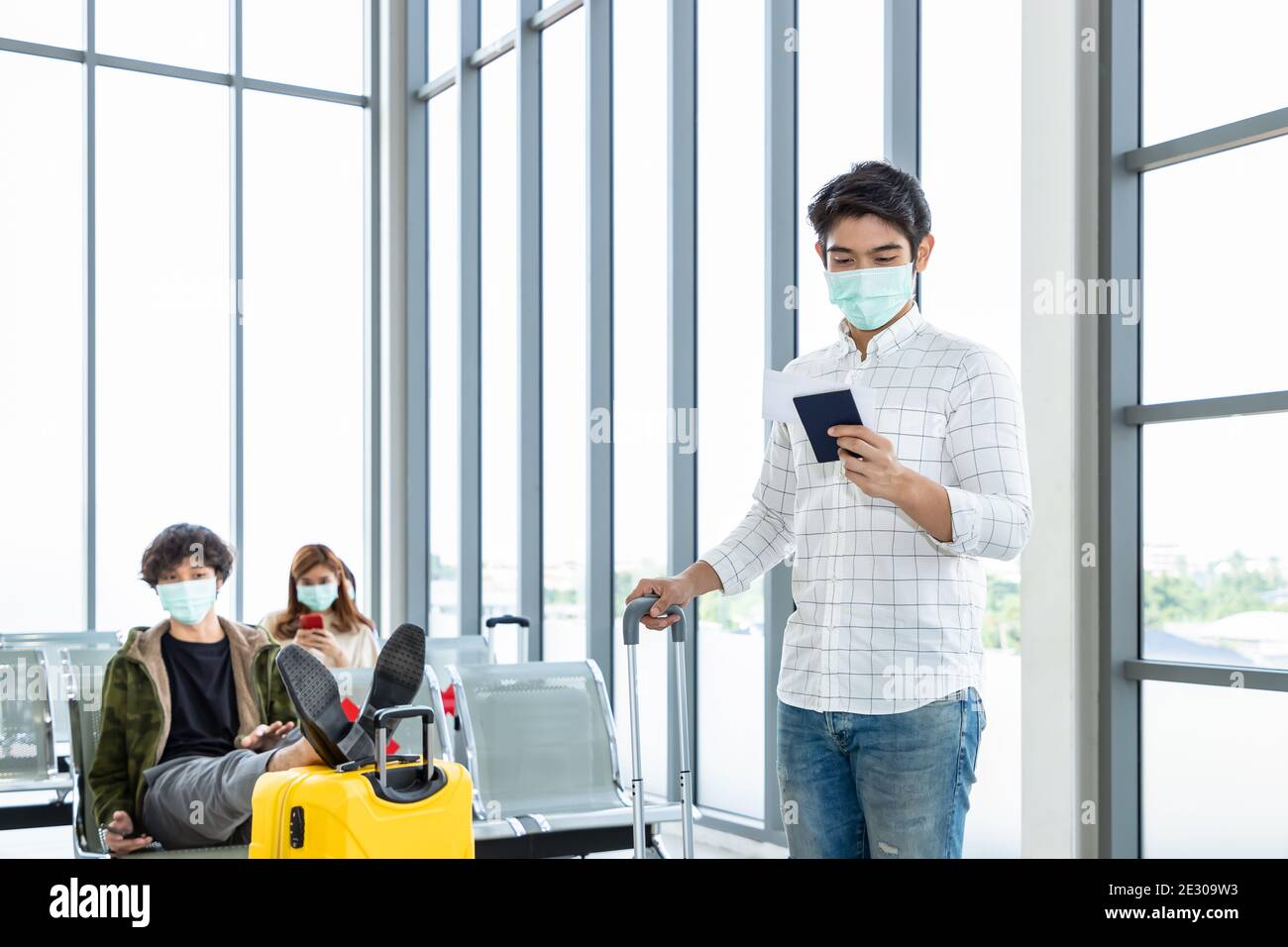 Traveler wearing protective mask in airport, during Covid-19 pandemic, with social distancing protocol. Checking passport and document to prepare to t Stock Photo