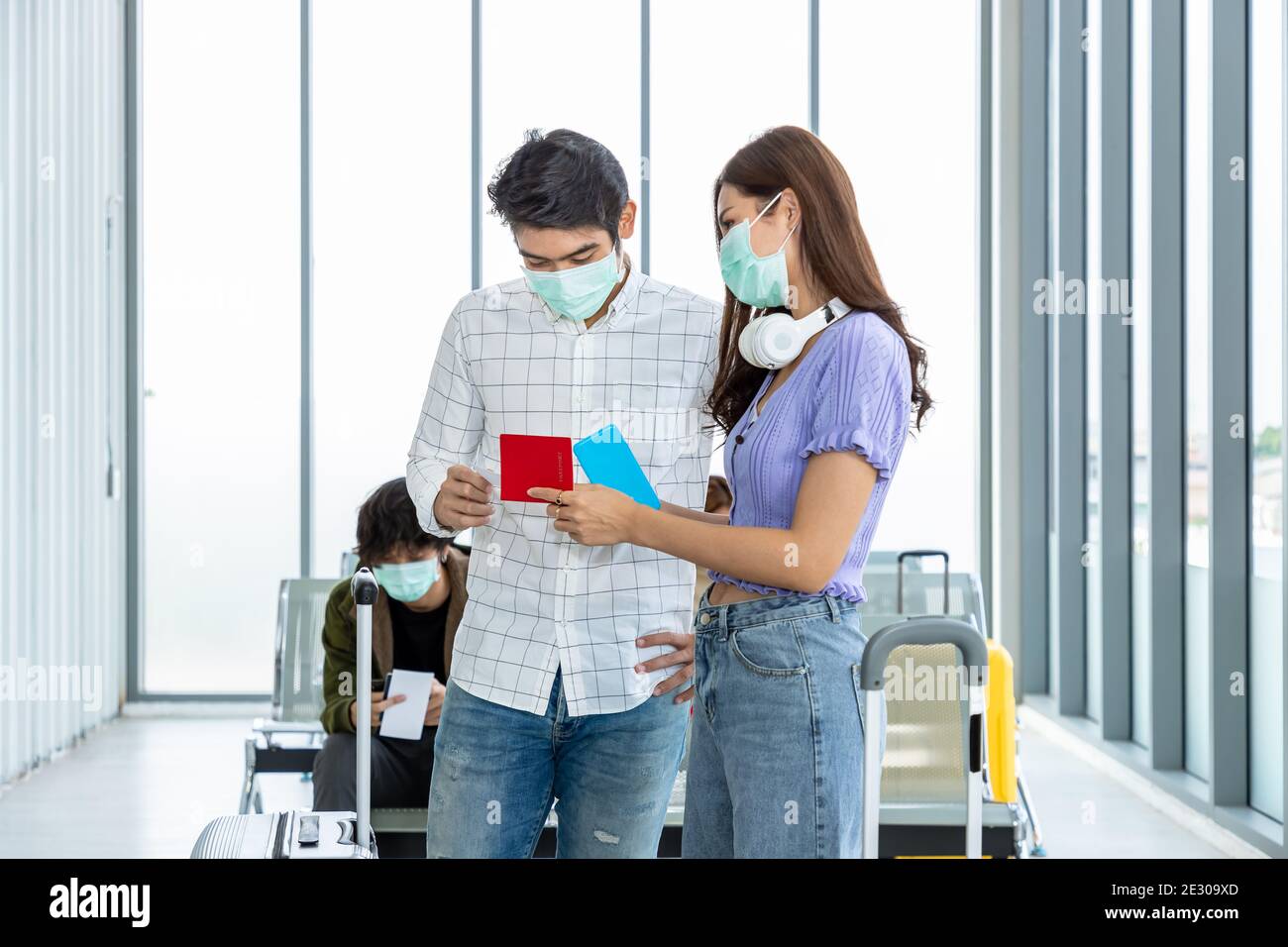 Couple travelers wearing protective mask in airport, during Covid-19 pandemic, with social distancing protocol. Holding passport and document preparin Stock Photo