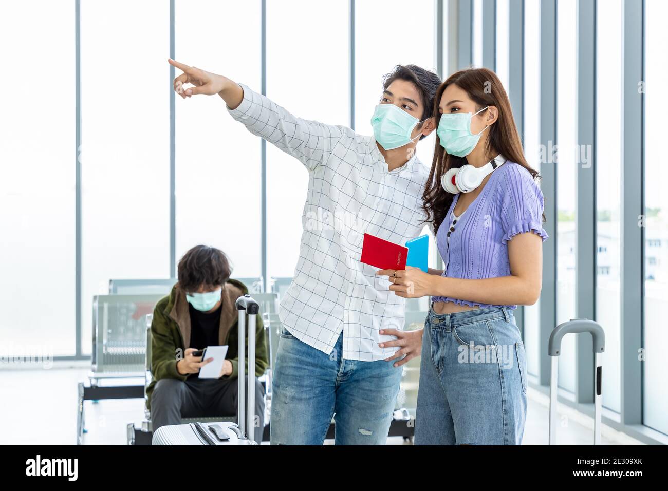 Couple travelers wearing protective mask in airport, during Covid-19 pandemic, with social distancing protocol. Holding passport and document preparin Stock Photo