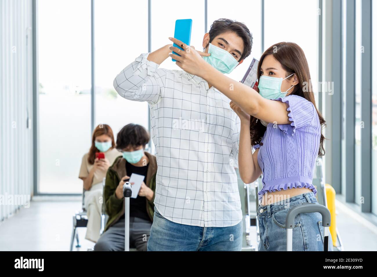 Couple travelers wearing protective mask in airport, during Covid-19 pandemic, with social distancing protocol. Taking photo and selfie before, prepar Stock Photo