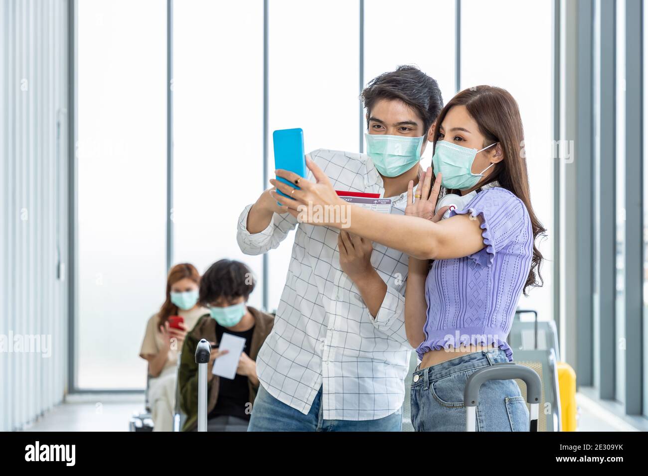 Couple travelers wearing protective mask in airport, during Covid-19 pandemic, with social distancing protocol. Taking photo and selfie before, prepar Stock Photo