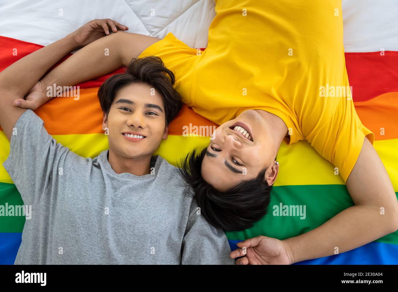 Happy Asian homosexual gay couple lying on rainbow pride flag. LGBT concept. Looking at camera. Stock Photo