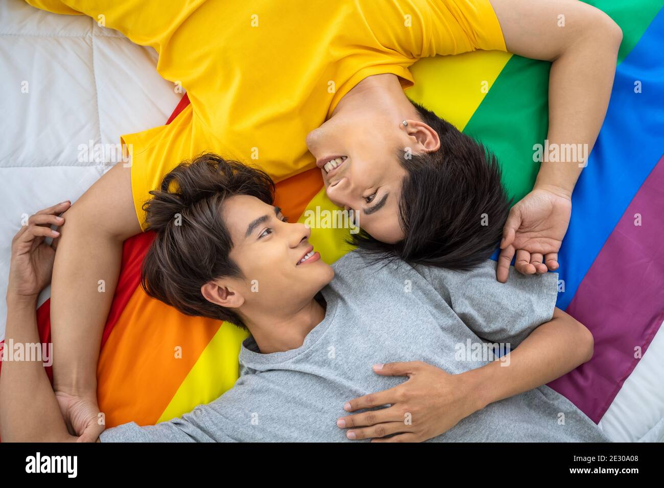Happy Asian homosexual gay couple lying on rainbow pride flag. LGBT concept. Stock Photo