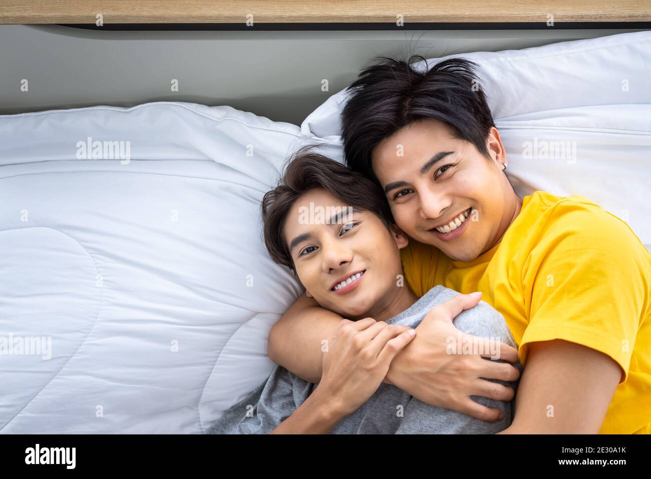 Happy Asian homosexual gay men male couple lying and embracing on bed. LGBT and sexual diversity concept. Looking at camera. Stock Photo