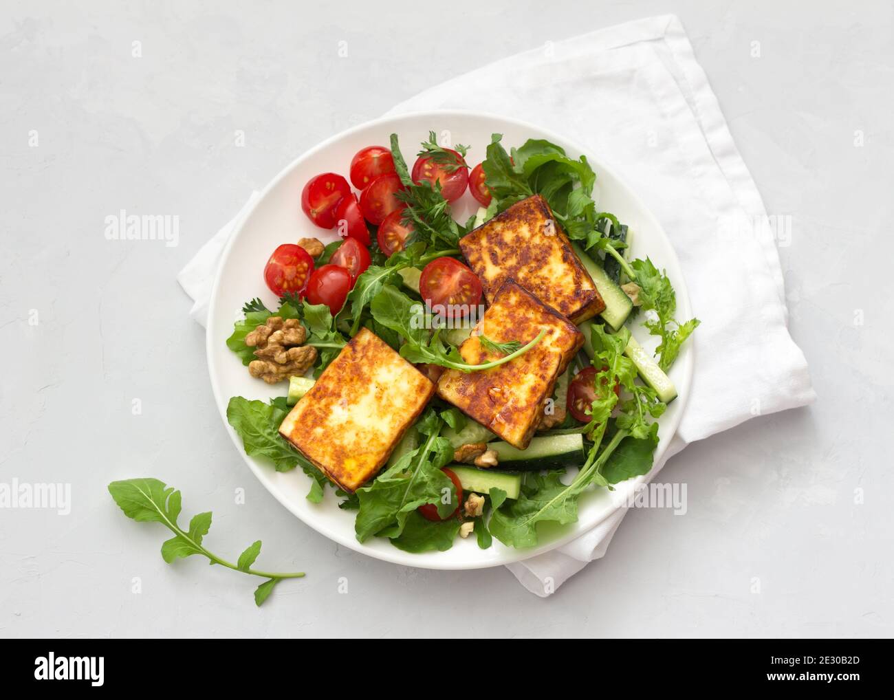 Fresh salad from arugula, cherry tomatoes, cucumbers and roasted cheese on a gray stone background. top view. delicious healthy food Stock Photo