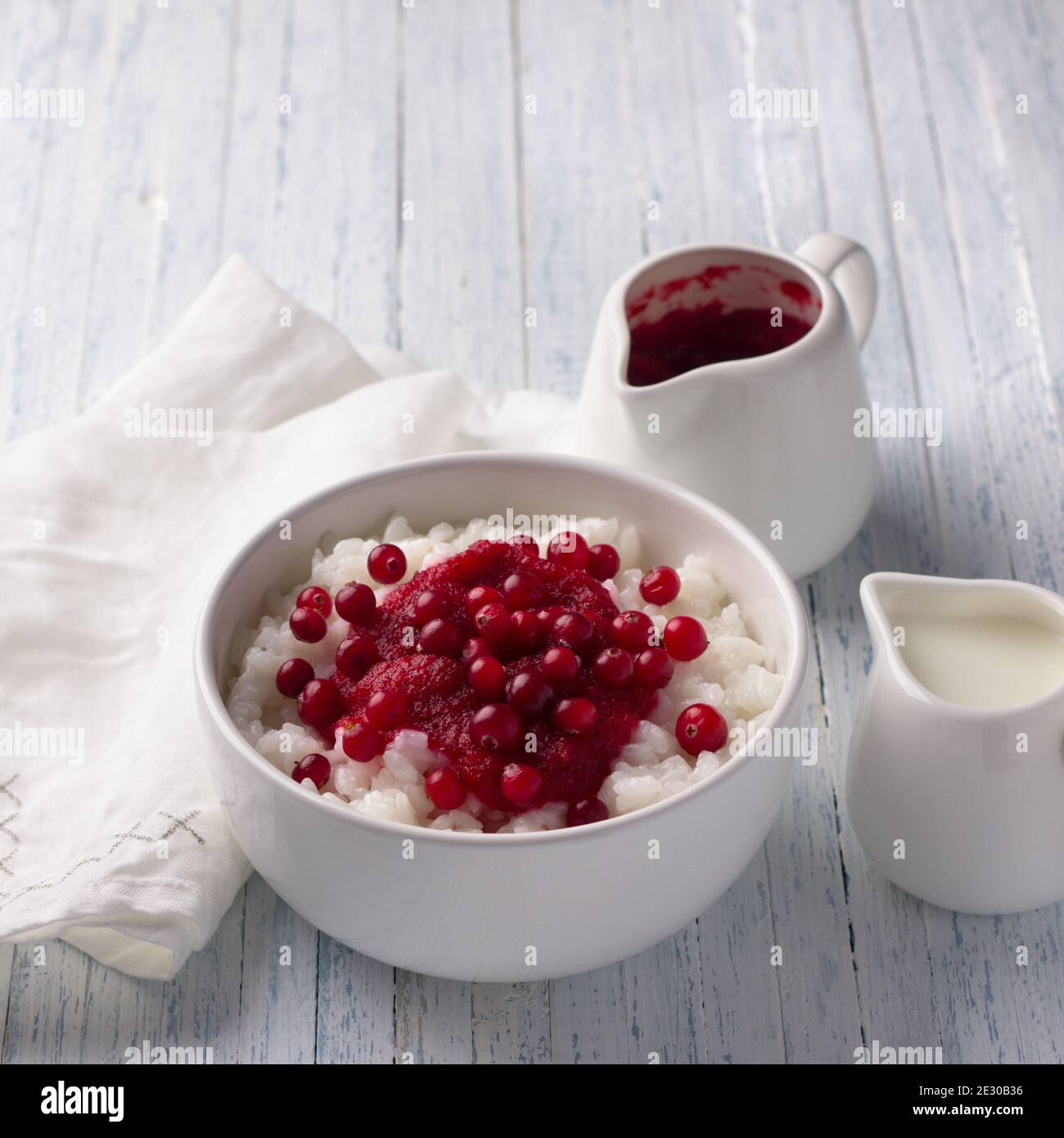 Delicious rice pudding with cranberry jam and fresh cranberries in a white bowl on a light blue background, selective focus Stock Photo