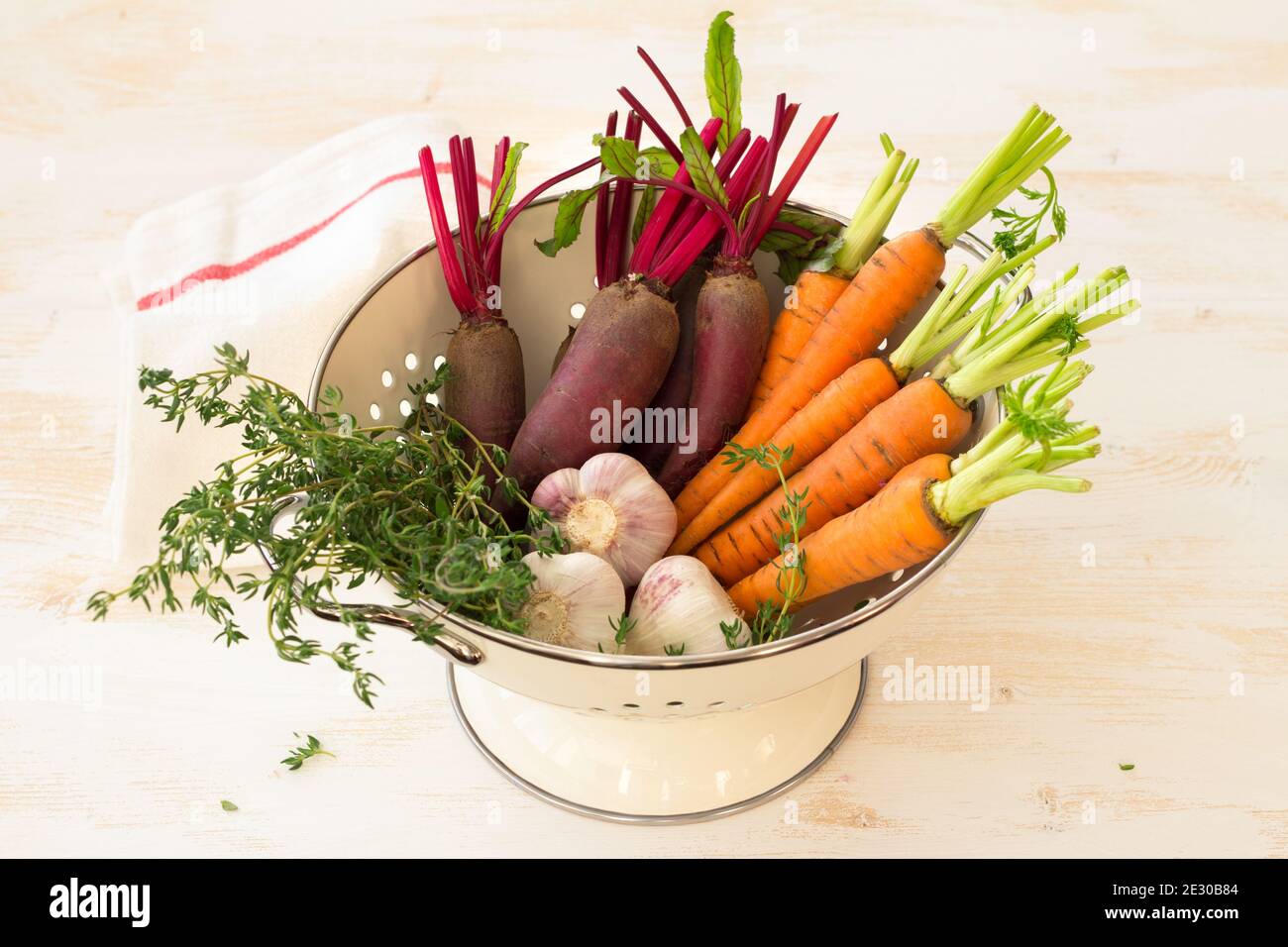 Fresh young organic vegetables, carrots, beets, garlic and greens for salad in colander on white background, selective focus. Healthy vegan food Stock Photo
