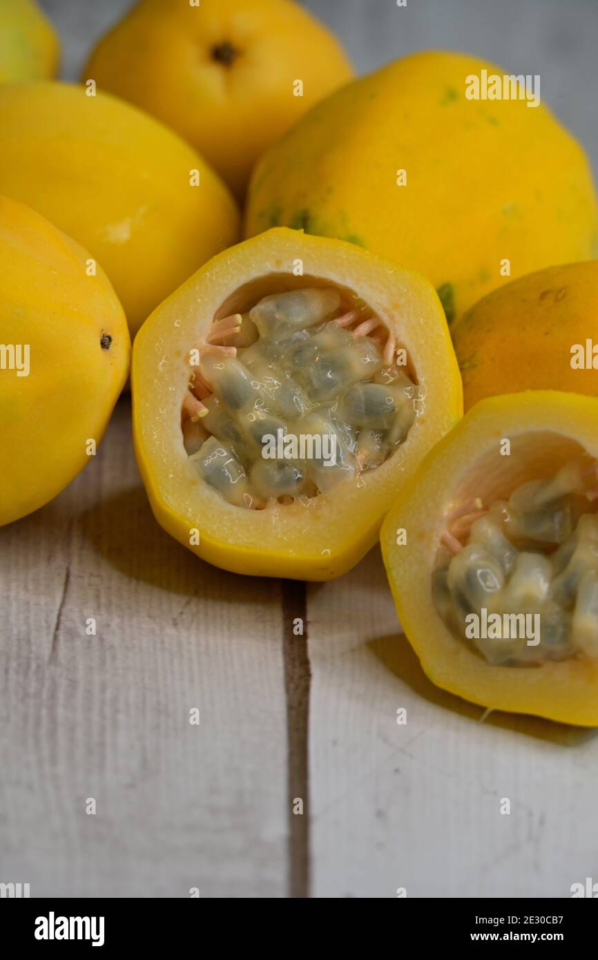 Whole and cut yellow passion fruit, Passiflora edulis, with its distinctive rind and numerous tiny, dark brown or black, pitted seeds, on table top Stock Photo