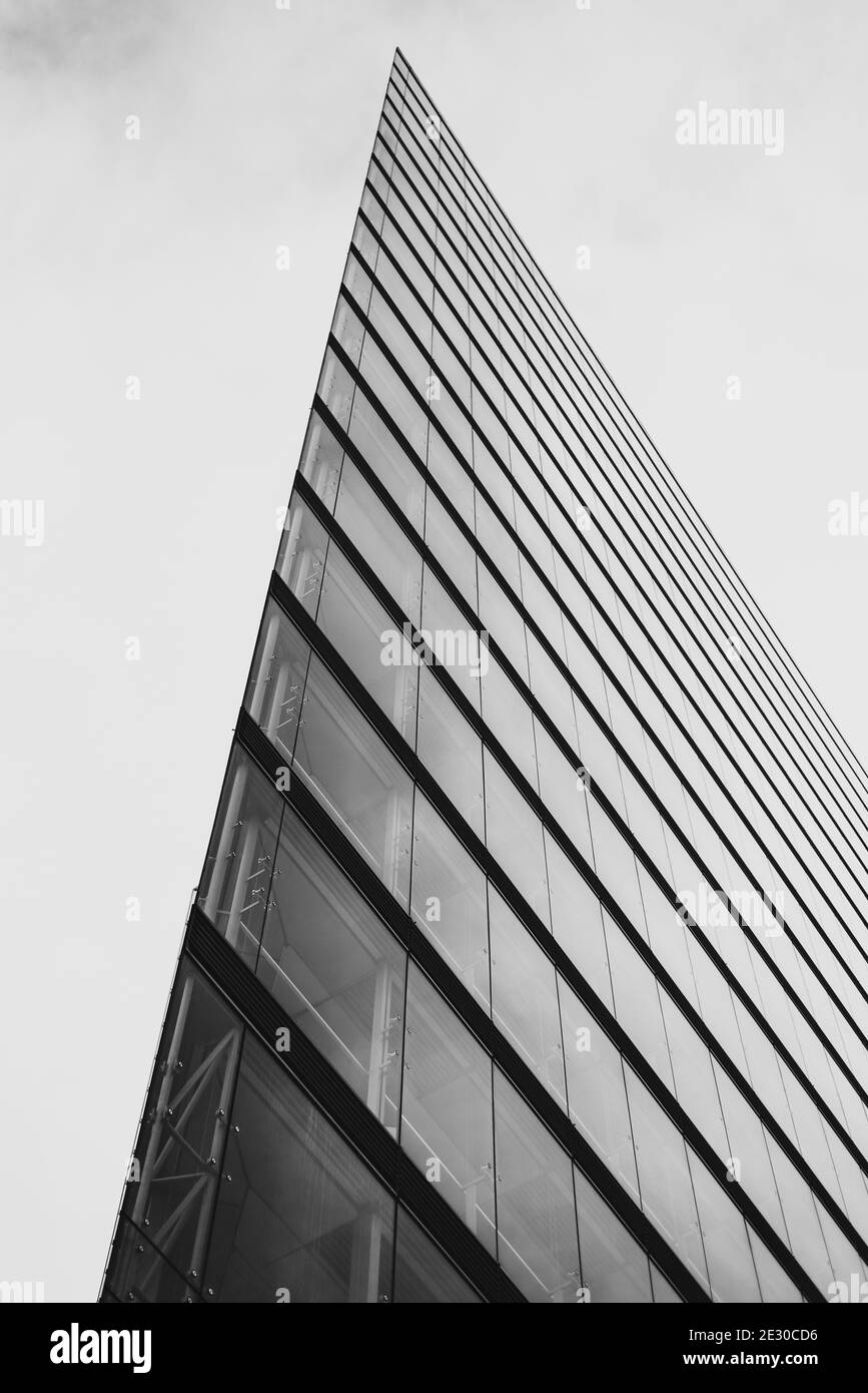 Vertical grayscale shot of a righ-rise modern glass-made office building sharp corner Stock Photo
