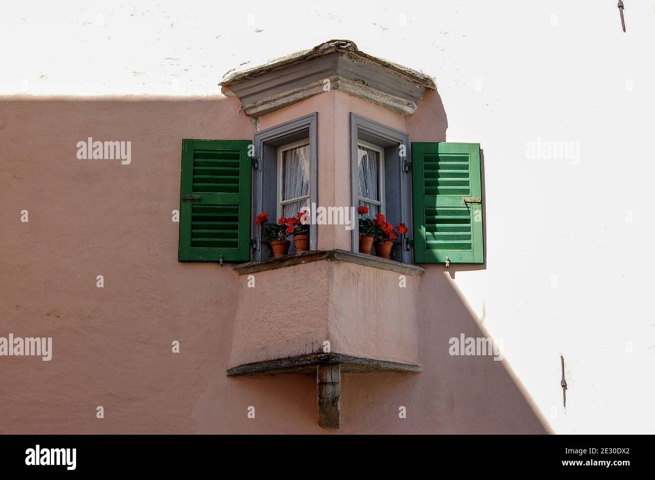 Small old balcony with wooden windows and red geraniums in the small town of Tirano, Italian Alps, Valtellina, Sondrio province, Lombardy, Italy, Eu. Stock Photo