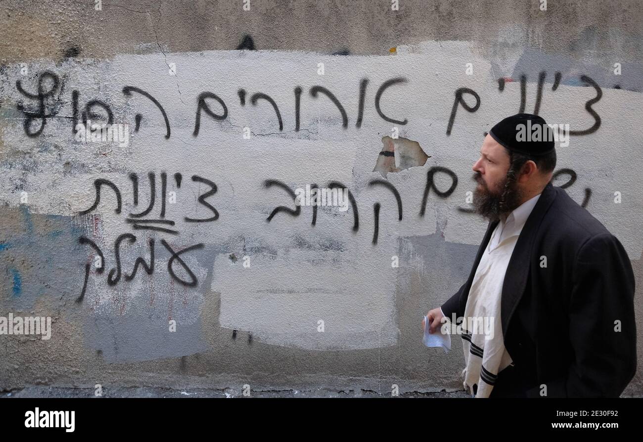 An ultra orthodox Jew walks past a wall with anti Zionism hate graffiti sprayed by extreme anti-Zionist Haredi Jews in Mea Shearim ultra orthodox neighborhood in West Jerusalem Israel. Neturei Karta opposes Zionism and calls for a 'peaceful dismantling' of the State of Israel, in the belief that Jews are forbidden to have their own state until the coming of the Jewish Messiah and that the state of Israel is a rebellion against God. Stock Photo