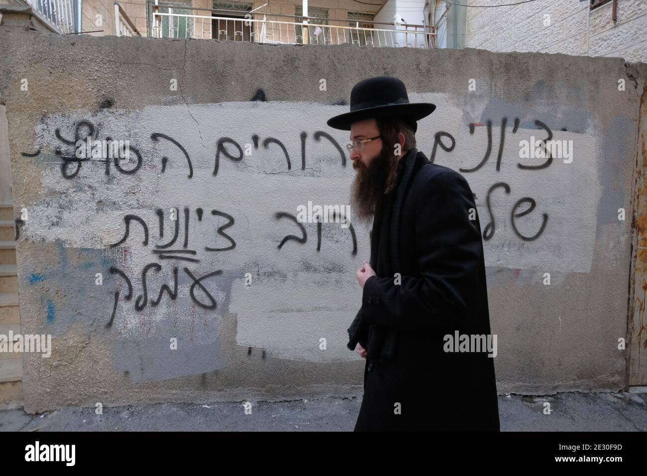 An ultra orthodox Jew walks past a wall with anti Zionism hate graffiti sprayed by extreme anti-Zionist Haredi Jews in Mea Shearim ultra orthodox neighborhood in West Jerusalem Israel. Neturei Karta opposes Zionism and calls for a 'peaceful dismantling' of the State of Israel, in the belief that Jews are forbidden to have their own state until the coming of the Jewish Messiah and that the state of Israel is a rebellion against God. Stock Photo