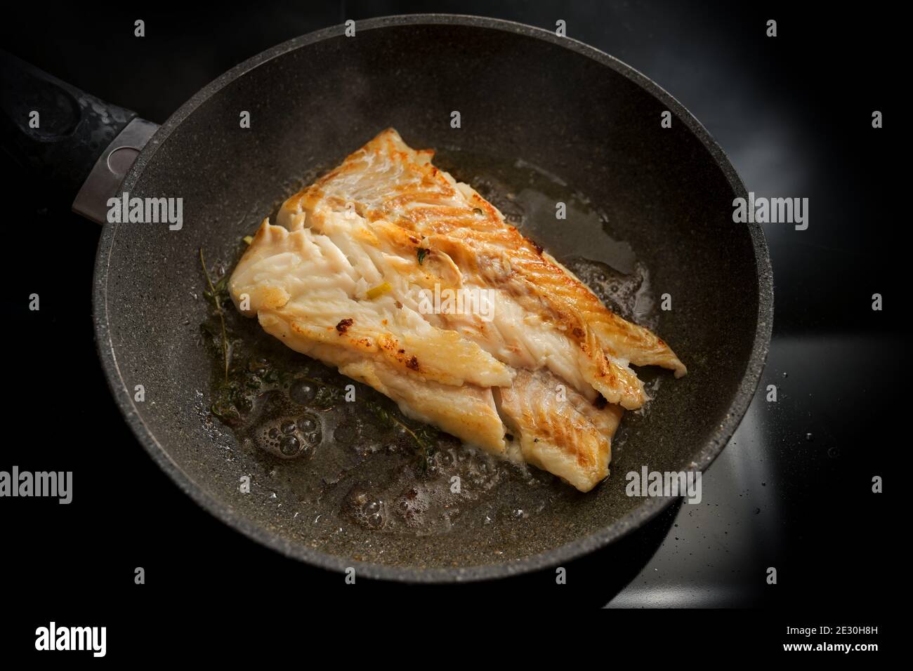 Cod fish fillet sautéed in butter in a frying pan on the stove, selected focus, narrow depth of field Stock Photo