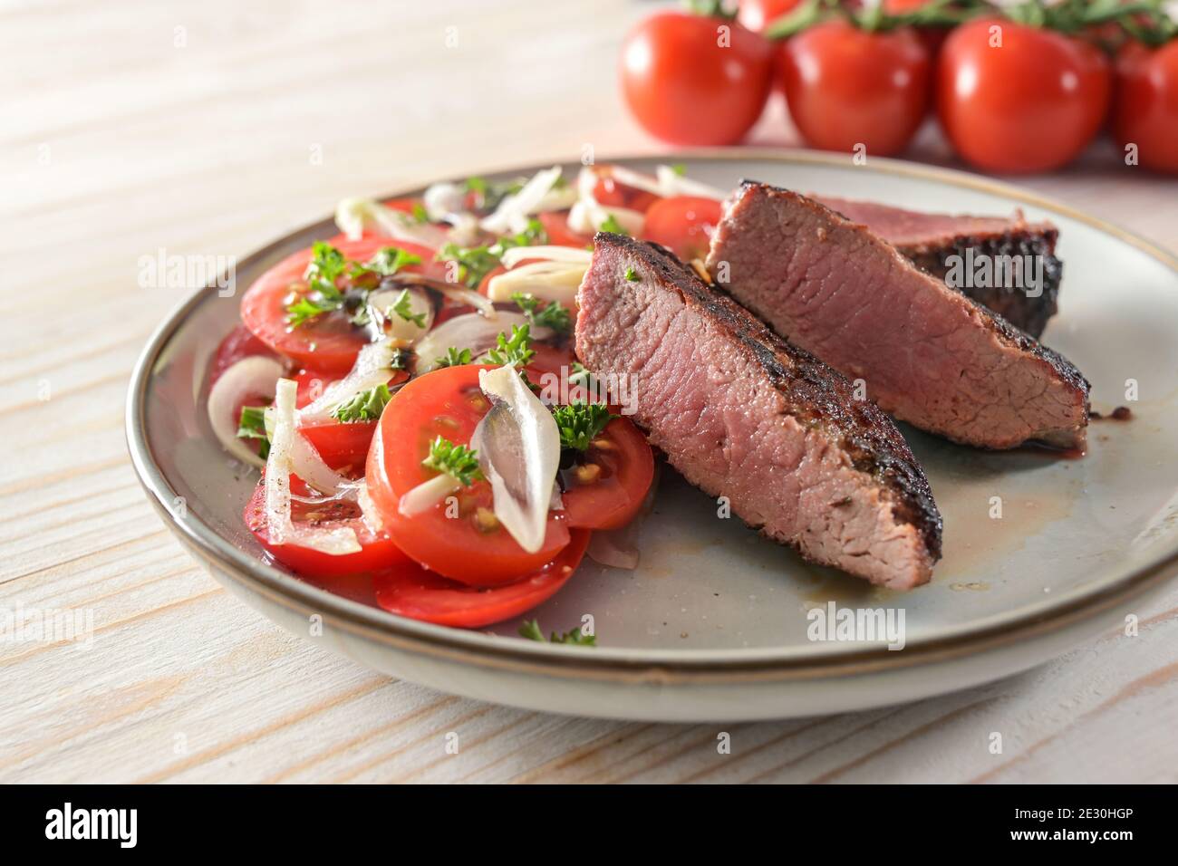 Roasted lamb fillet with tomato salad, onions and parsley garnish on a plate, selected focus, narrow depth of field Stock Photo