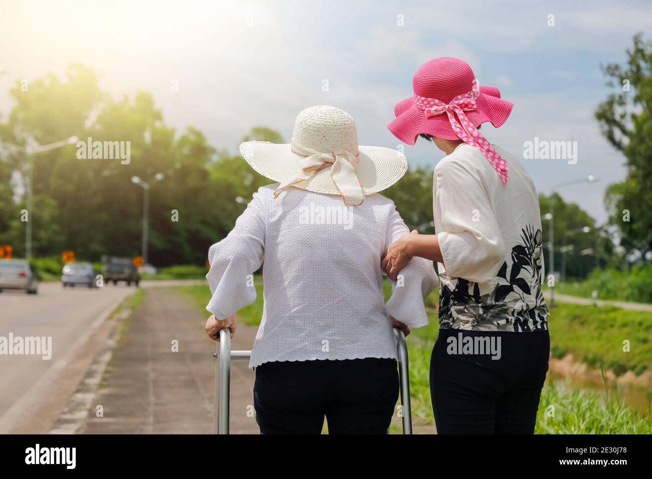Daughter take care elderly woman walking on street in strong sunlight. Stock Photo