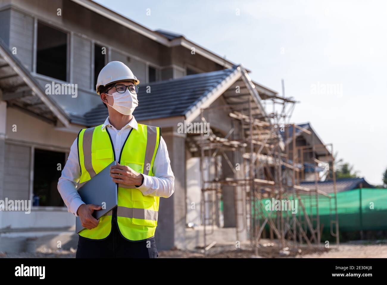 Portrait of Architect wearing a mask hold a laptop on a building construction site, Homebuilding Ideas and Prevention of Coronavirus Disease. Stock Photo