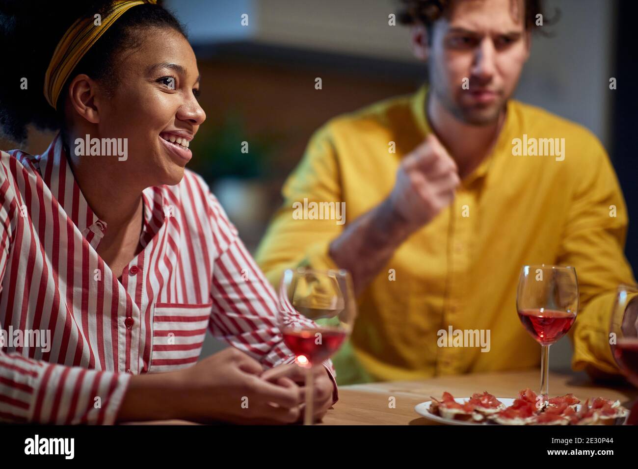 Pretty mixed couple relaxing and drinking wine together at home Stock Photo