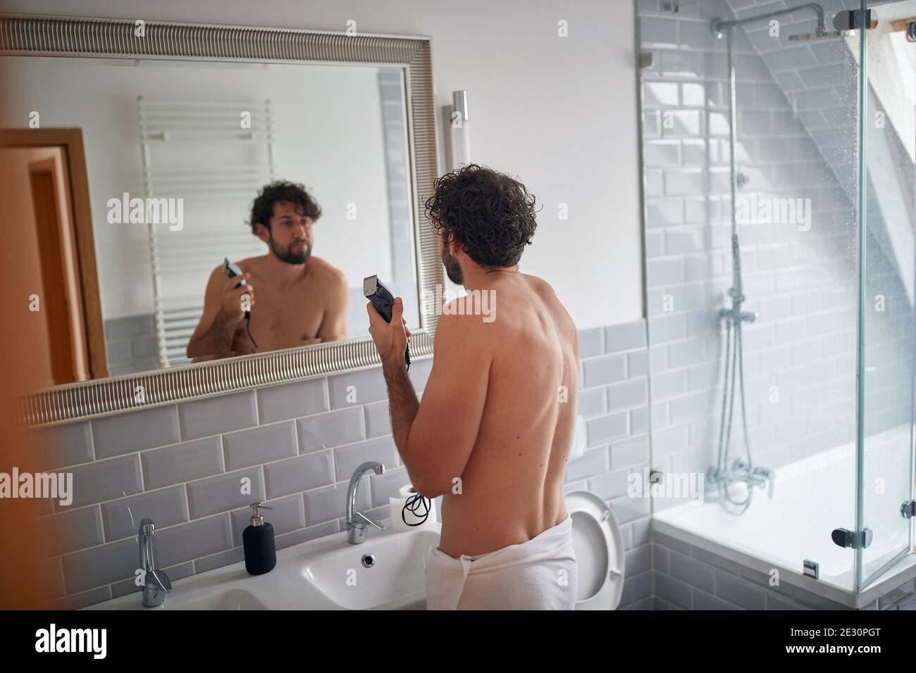 Caucasian topless man shaving with shaver in the bathroom Stock Photo