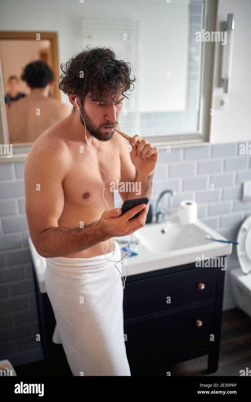 Young handsome man having a call while brushing teeth on a beautiful morning in the bathroom. Hygiene, bathroom, morning Stock Photo
