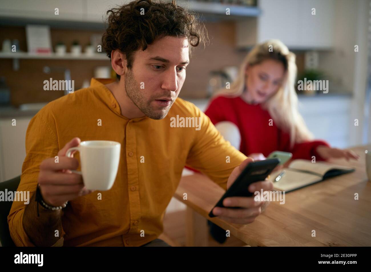 A young couple enjoying a coffee and surfing the internet on a beautiful morning at the kitchen. Routine, relationship, together Stock Photo